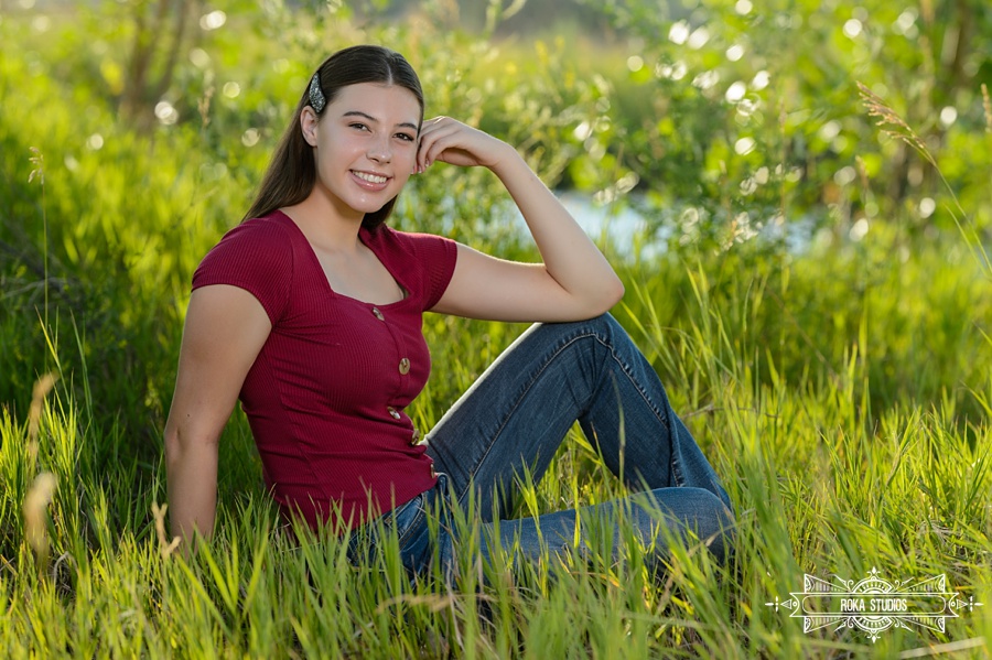 Loveland Senior pictures of a girl sitting in a golden field of greenery. 