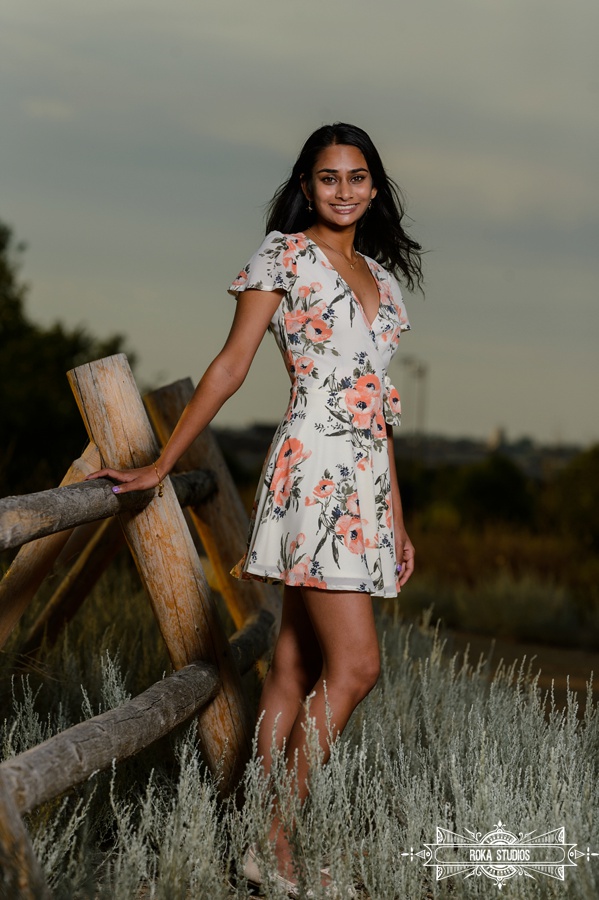 Senior girl next to rustic fence line in a floral dress. 