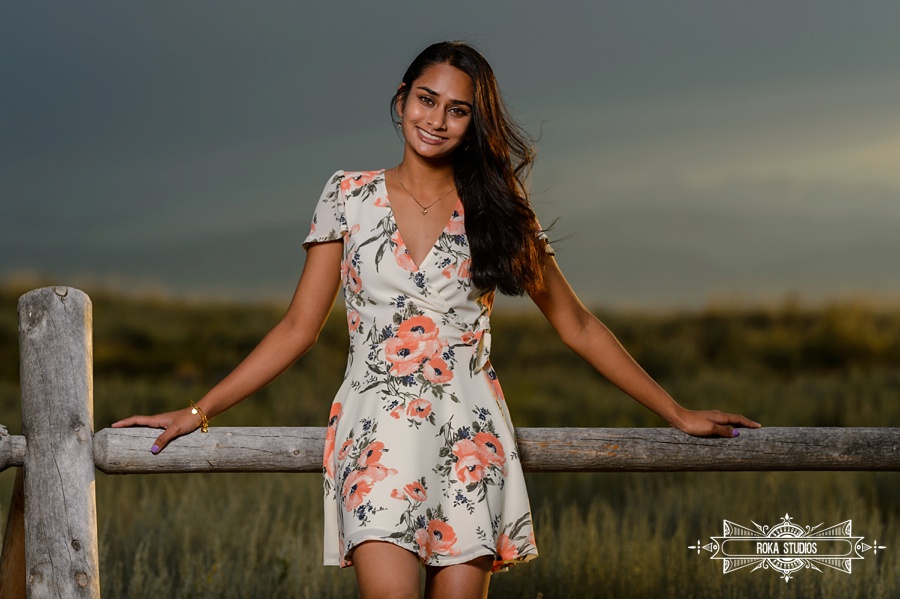 Senior pictures of a girl in front of rustic wood fence in a floral dress. 